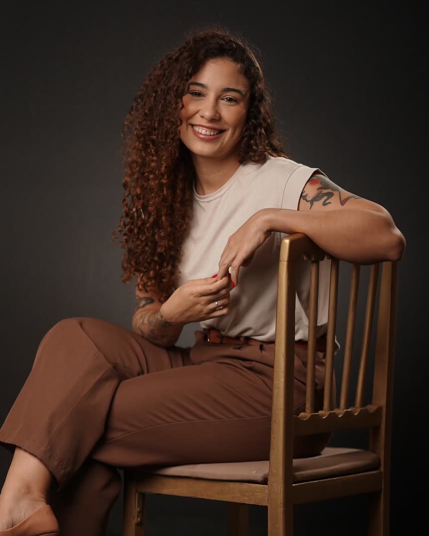 Leilane Falcão, psicóloga, sorrindo, sentada numa cadeira de madeira